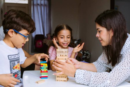 International Children Day and Family Day. Latin mother having fun with her children at *home* with blocks on white table. Single mother of two young children, responsible and happy. Concept of love.