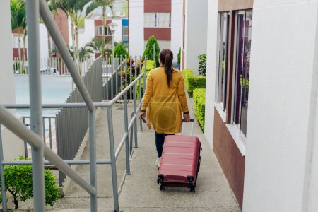 Mujer latina feliz con su maleta rosa de vacaciones. Mujer emocionada lista para viajar y disfrutar del verano. Felicidad y viajes.