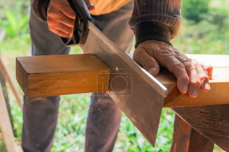 Téléchargez les photos : Homme plus âgé travaillant à la maison avec une scie à main. Latino couper le bois et réparer. Outils de menuiserie. - en image libre de droit
