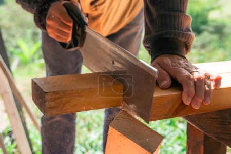 Téléchargez les photos : Homme plus âgé travaillant à la maison avec une scie à main. Latino couper le bois et réparer. Outils de menuiserie. - en image libre de droit