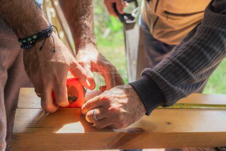 Téléchargez les photos : Hommes mesurant le bois avec flexomètre à couper à la scie à main. Les Latinos travaillent à la maison. Outils de menuiserie. Père et fils. - en image libre de droit