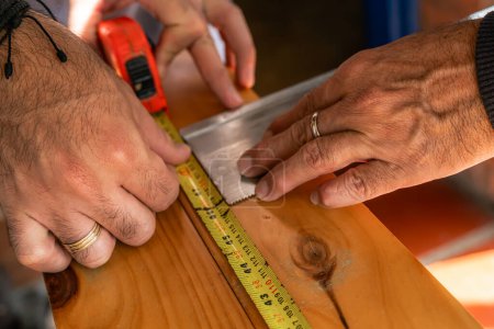 Téléchargez les photos : Hommes mesurant le bois avec flexomètre à couper à la scie à main. Les Latinos travaillent à la maison. Outils de menuiserie. Père et fils. - en image libre de droit