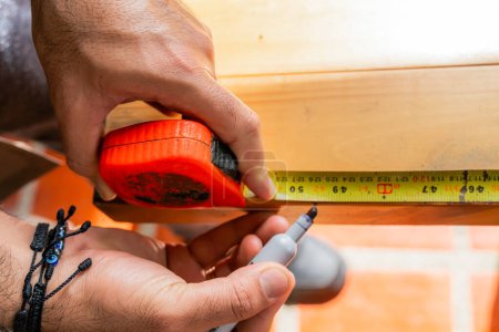 Téléchargez les photos : Homme mesurant le bois avec flexomètre et marquage au crayon travaillant dans sa maison. Latino dans son atelier. - en image libre de droit