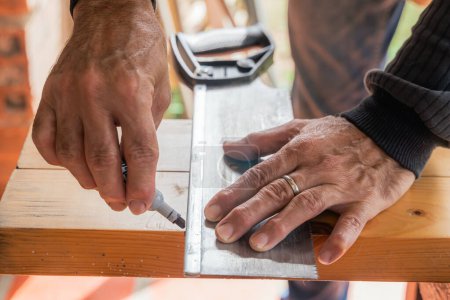 Téléchargez les photos : Homme plus âgé travaillant à la maison avec une scie à main. Latino couper le bois et réparer. Outils de menuiserie. Main avec anneau au premier plan. Espace de copie. - en image libre de droit
