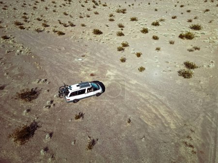 Foto de Vista aérea del vehículo recreativo autoconvertido autocaravana van conduciendo en un lecho de lago seco en el desierto del sur de Nevada Estados Unidos con paneles solares y bicicletas montadas en la plataforma de vida van rv. - Imagen libre de derechos