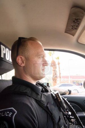 Téléchargez les photos : Vertical image of white male caucasian police officer driving in his vehicle in his city investigating a possible situations in the city on a warm afternoon. Patrolling daytime. - en image libre de droit