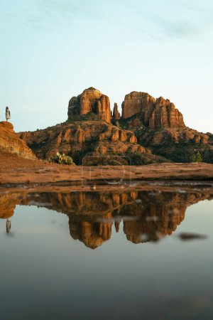 Téléchargez les photos : Young beautiful woman standing on rock point looking out at Cathedral Rock in Sedona Arizona USA Southwest with incredible sunset colors and beautiful reflection from small pool of water on red stone. - en image libre de droit