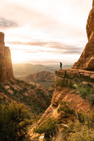 Téléchargez les photos : Jeune homme se tient regardant vers le bas falaise dramatique au coucher du soleil à Cathedral Rock Sedona - en image libre de droit