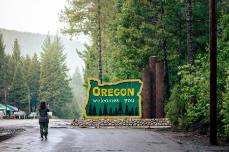 Téléchargez les photos : Femme, trentaine, prend une photo de l'Oregon vous accueille signe à la ligne d'état US-HWY 199. - en image libre de droit