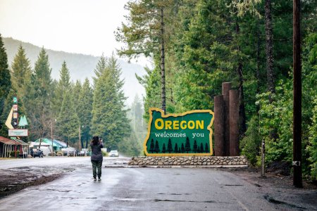 Téléchargez les photos : Femme, 30s, prend une photo de l'Oregon vous accueille signe sur Redwood Highway. - en image libre de droit