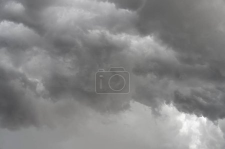 Dark, brooding storm clouds loom overhead, poised to release their downpour. The photograph captures a turbulent sky filled with dark gray storm clouds. Within their shadowed interiors, smaller cloud formations swirl and shift shapes. 
