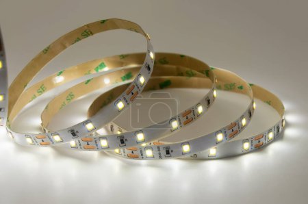 Discover versatility of modern lighting with illuminated LED strip light coils. White glowing LED tape, arranged in circular shapes, showcases flexibility and innovation of contemporary lighting solutions, perfect for adding ambiance to any space.