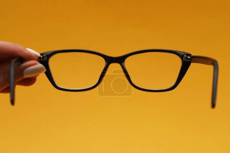Brille mit Dioptrien in schwarzem Rahmen auf orangefarbenem Hintergrund. Geringe Tiefenschärfe