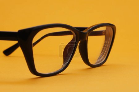 Brille mit Dioptrien in schwarzem Rahmen auf orangefarbenem Hintergrund. Geringe Tiefenschärfe