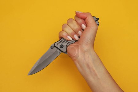 Foto de Cuchillo plegable en una mano femenina sobre un fondo naranja. Primer plano - Imagen libre de derechos