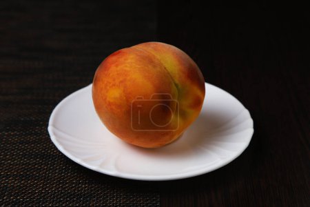 Appetizing peach on a white plate under dark lighting. Close-up