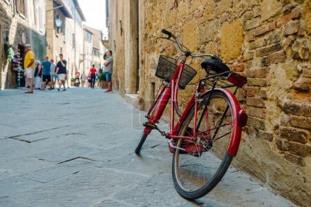 Foto de Pienza, Toscana: Bicicleta roja apoyada en una vieja pared a lo largo de la calle - Imagen libre de derechos