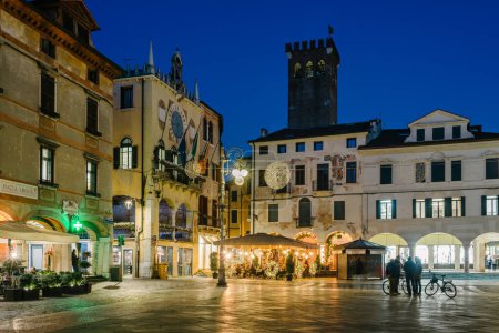 Téléchargez les photos : Bassano del Grappa, Italie - janvier 09, 2024 : Piazza Liberta ', Personnes et tables de café le soir en hiver. - en image libre de droit