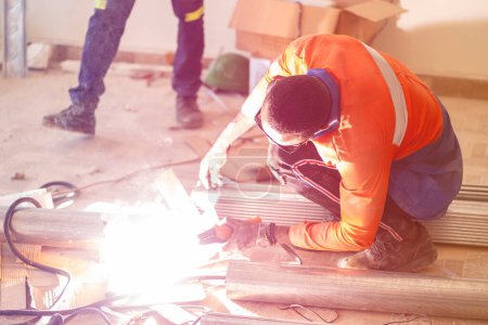 Photo pour Image étincelante de l'homme africain tenant un équipement de soudage dans un environnement de travail- concept de fabrication de métaux - image libre de droit