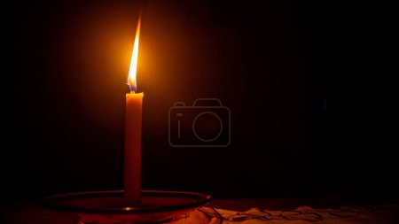 eine brennende Kerze vor dunklem Hintergrund