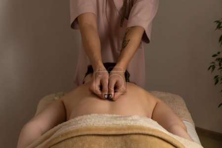 Téléchargez les photos : Masseur fait un massage du dos debout à la tête d'une femme couchée sur un canapé de massage dans une atmosphère chaleureuse. Concept de spa, santé. - en image libre de droit