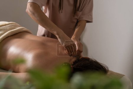 Téléchargez les photos : Gros plan des mains du masseur massant le dos d'une femme dans le salon dans une ambiance chaleureuse. Concept d'un mode de vie sain et de soins du corps. - en image libre de droit