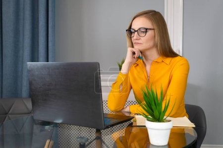 Junge Psychologin in orangefarbener Bluse und Brille sitzt an einem Glastisch und führt eine Online-Beratung in einem psychologischen Zentrum durch.