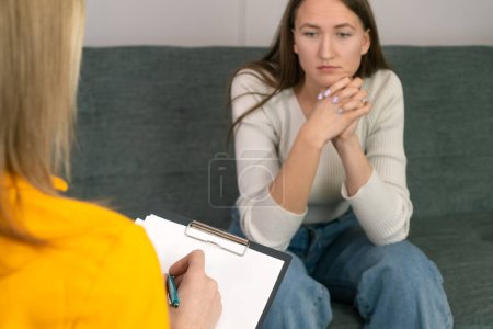 Jeune femme aux yeux perplexes lors d'une réception avec un psychologue-consultant. Le client parle de problèmes. Conversation avec un thérapeute, conseils, aide.