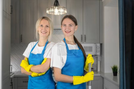 Photo for Two young beautiful smiling women in aprons are standing shoulder to shoulder with their arms crossed on their chests looking at the camera. Conceptual advertising of a cleaning company - Royalty Free Image