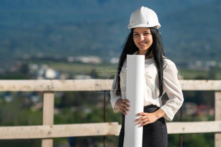 Photo for Young female engineer in a white helmet, engaged in the development of plans to ensure the safety of equipment. Concept of building, development, construction and architecture. - Royalty Free Image