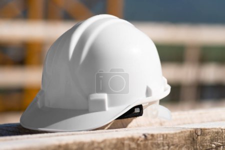Photo for Close-up of a white helmet lying on a wooden beam on a construction site on a sunny day. Security concept - Royalty Free Image