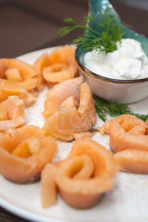 Gros plan de morceaux de saumon marinés sur une assiette blanche avec sauce et aneth sur la table. Belle portion de saumon mariné. Photo verticale
