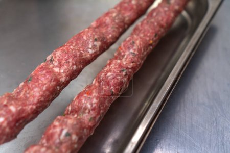 Primer plano de un kebab de lula crudo con especias en pinchos en una bandeja de metal en la mesa, enfoque selectivo