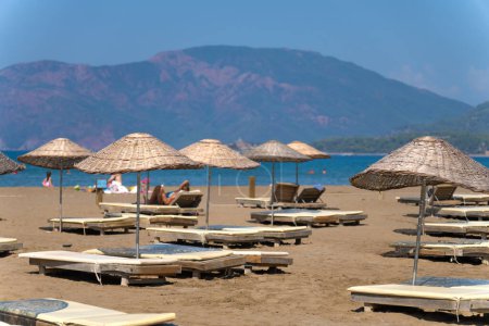 Sun loungers and umbrellas on Iztuzu beach on a sunny day against the background of mountains, Turtle beach, Mediterranean Sea, Marmaris, Turkey