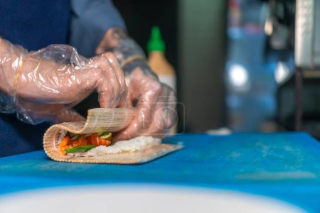 Téléchargez les photos : Close-up chef en gants prépare des rouleaux de sushi sur un tableau bleu dans la cuisine, copier l'espace. Processus de fabrication des sushis - en image libre de droit