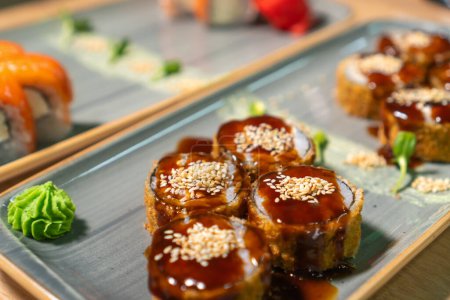 Close-up of delicious hot Banzai sushi with rice, cream cheese, salmon, panko, sesame seeds, teriyaki sauce on a beautiful rectangular dish. Concept of traditional Japanese food
