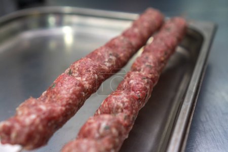 Close-up of a raw lula kebab with spices on skewers on a metal tray on the table, selective focus