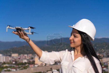 Foto de Una joven especialista en sombreros lanza un dron en un sitio de construcción en un día soleado. Arquitectura, gestión de proyectos, ingeniería civil, inspección de edificios. - Imagen libre de derechos