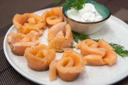 Close-up of pickled salmon pieces on a white plate with sauce and dill on the table. Beautiful serving of pickled salmon