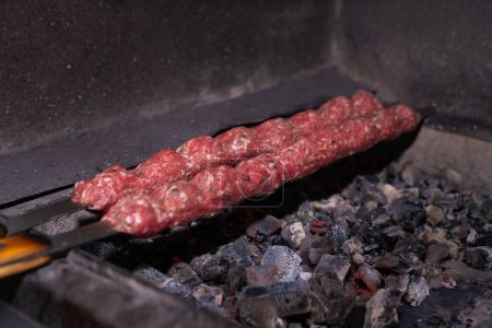 Primer plano de un kebab crudo con especias en pinchos se cocina sobre carbones con humo, enfoque selectivo