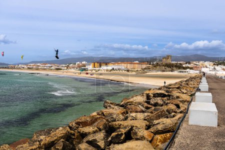 Foto de Kitesurfistas cabalgando sobre el océano cerca de la playa con Tarifa ciudad en el fondo. Andalucía, España. Soleado y ventoso día de primavera. - Imagen libre de derechos