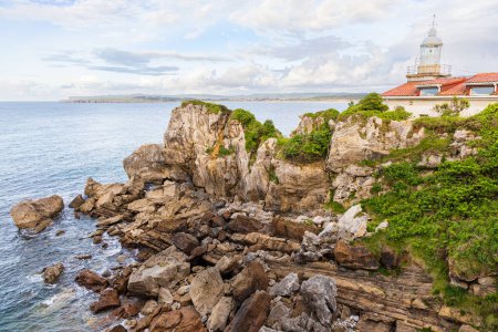 Photo for Cliffs partially covered with shrubs, the Atlantic Ocean and Faro de La Cerda lighthouse. Magdalena Peninsula, Santander, Cantabria, Spain. - Royalty Free Image