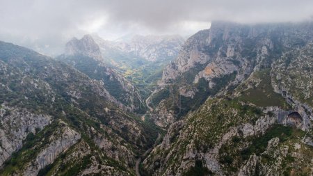 View of the narrow La Hermida gorge, the winding road through it, and the rugged peaks of Picos de Europa on a cloudy day with looming clouds, from the Jozarcu Viewpoint, also known as Santa Catalina Viewpoint. Cantabria, Spain.