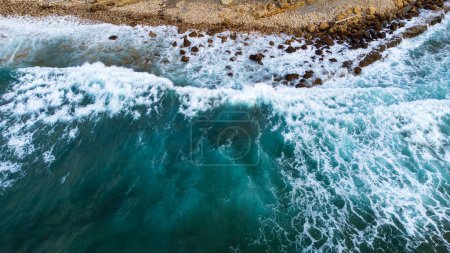 Foto de Una poderosa ola azul oscuro con espuma blanca chocando contra la costa rocosa. Vista aérea desde el lado del Océano Atlántico. Pielagos, Cantabria, España. - Imagen libre de derechos