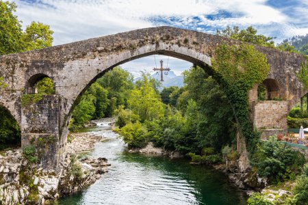 Roman bridge in Cangas de Onis or Pueton over the Sella River, with three slightly pointed arches and a symbol of Asturias placed in its central arch. Asturias, Spain.