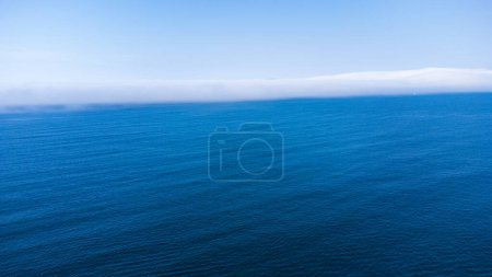 Aerial view of endless calm blue waters of the Atlantic Ocean and an approaching white cloud front. Sunny day. La Coruna, Galicia, Spain.