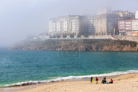 Téléchargez les photos : Orzn Beach, l'océan Atlantique, le front de mer et les bâtiments de La Coruna dans un brouillard épais. Journée ensoleillée. La Coruna, Galice, Espagne. - en image libre de droit