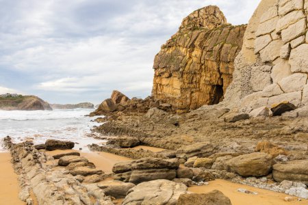 Portio Beach with its golden sand, layers of rock eroded since the Glaciation, the stormy Atlantic Ocean, and whimsical erosive, sedimentary rock formations. Costa Quebrada Geopark, Cantabria, Spain.