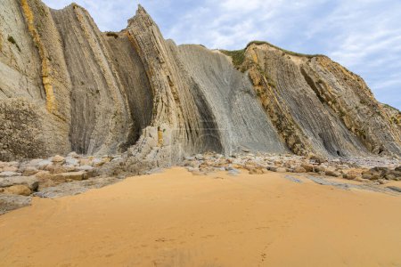 Whimsical erosive, sedimentary rock formations on Portio Beach with its golden sand. Costa Quebrada Geopark, Cantabria, Spain.