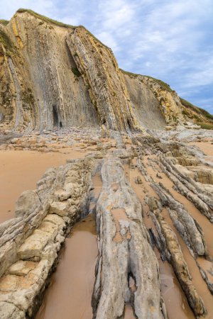 Whimsical erosive, sedimentary rock formations on Portio Beach with its golden sand and layers of rock. Costa Quebrada Geopark, Cantabria, Spain.